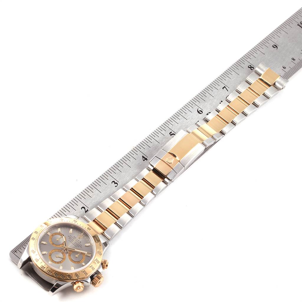 The image shows a Rolex Daytona 116523 Men's Steel and Gold (two tone) Grey Dial 116523 Men's Steel and Gold (two tone) Grey Dial watch, viewed from the top, displaying the face and band against a ruler.