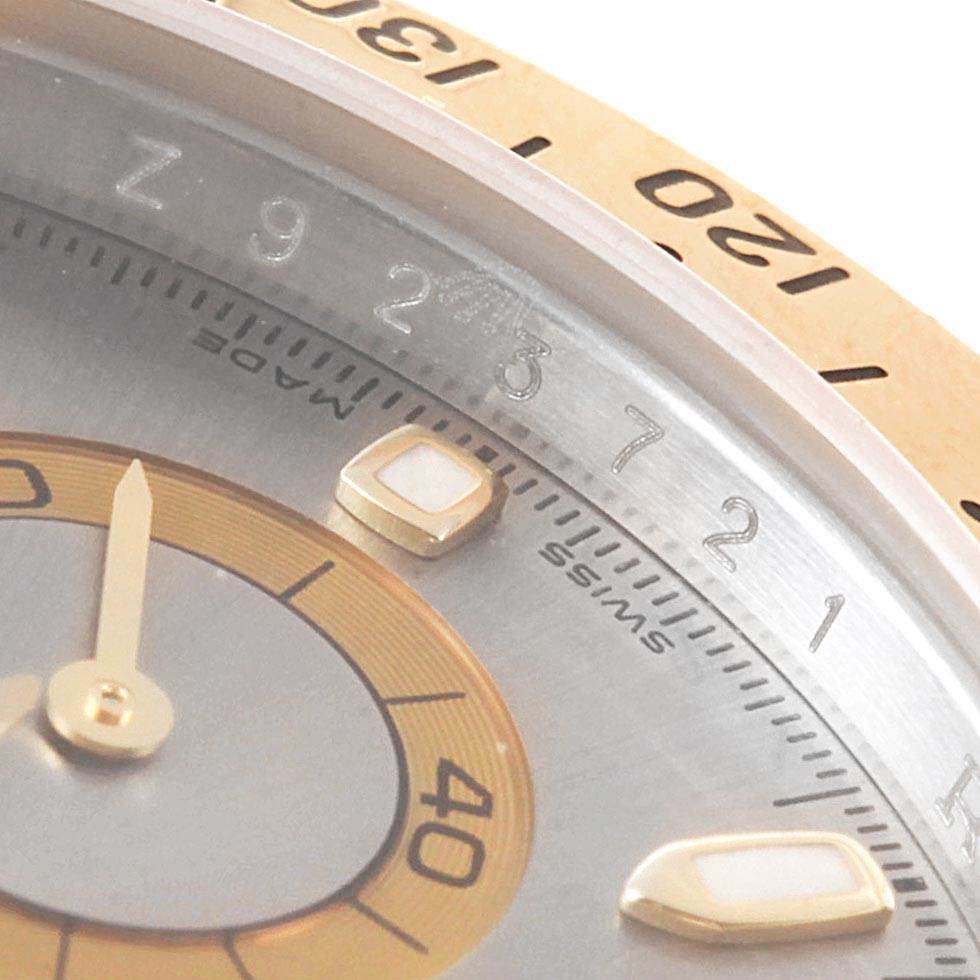 This is a close-up angle of the face and bezel of a Rolex Daytona 116523 Men's Steel and Gold (two tone) Grey Dial 116523 Men's Steel and Gold (two tone) Grey Dial watch, showcasing parts of its dial and markers.