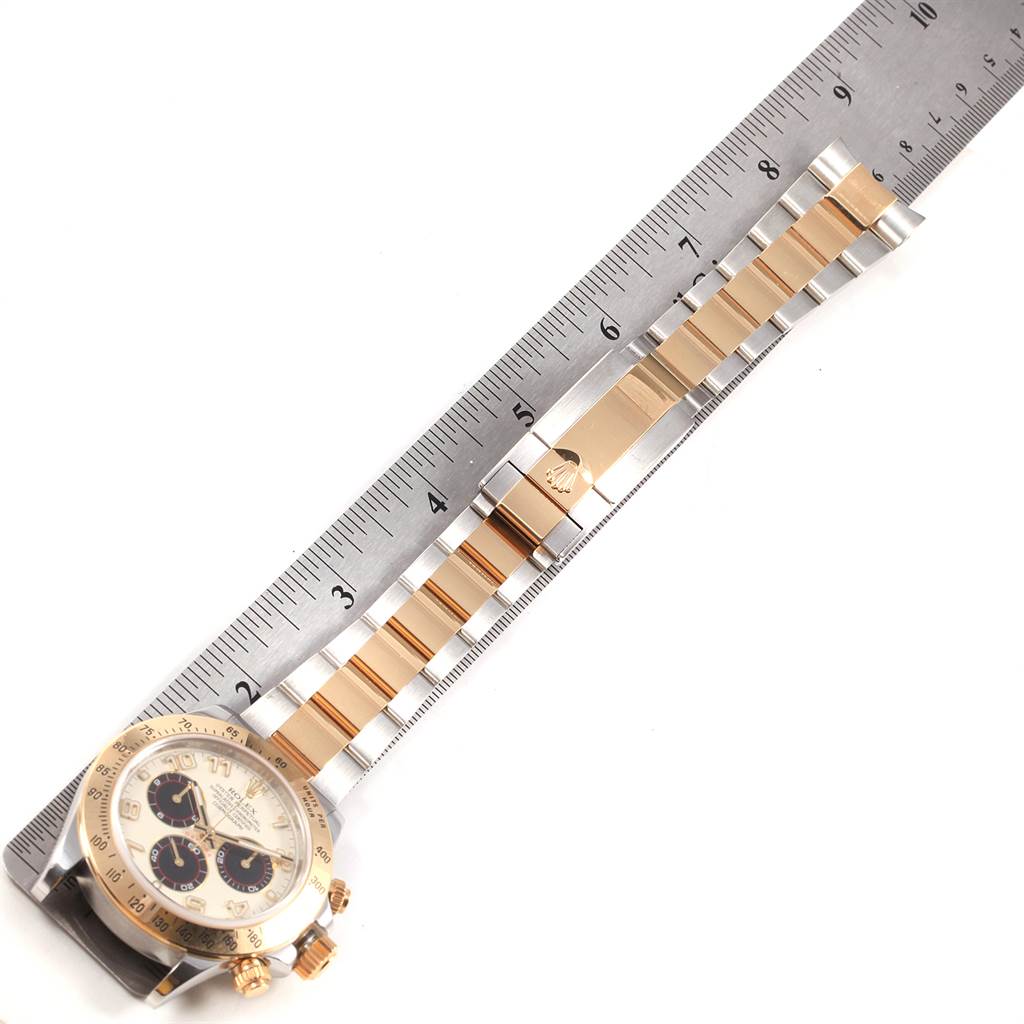 The Rolex Daytona 116523 Men's Steel and Gold (two tone) White Dial 116523 Men's Steel and Gold (two tone) White Dial watch is shown from above, displaying the face, bezel, and metal bracelet next to a ruler.