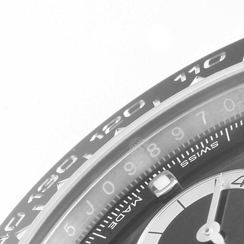 The image shows a close-up of the bezel, part of the dial, and the tachymeter scale of a Rolex Daytona 116500 Men's Stainless Steel Black Dial 116500 Men's Stainless Steel Black Dial watch.