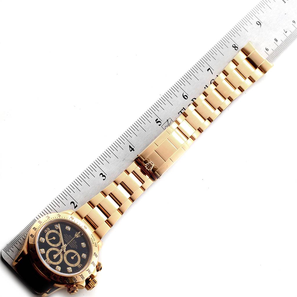 The image shows a Rolex Daytona 16528 Men's Yellow Gold Black Dial 16528 Men's Yellow Gold Black Dial watch laid flat next to a ruler, displaying its face and bracelet.