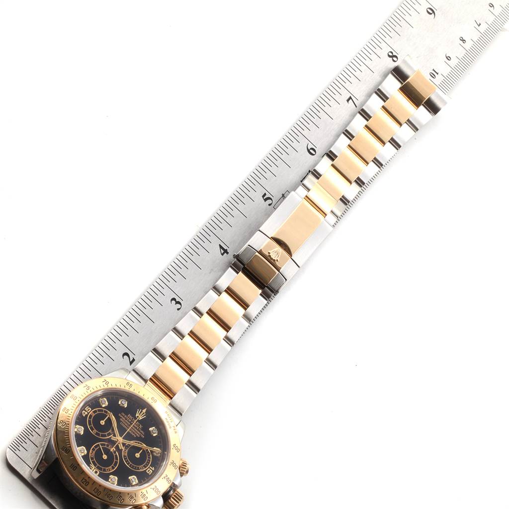 This image shows the Rolex Daytona 116523 Men
s Steel and Gold (two tone) Black Dial 116523 Men
s Steel and Gold (two tone) Black Dial watch laying flat, partially within the frame alongside a ruler.