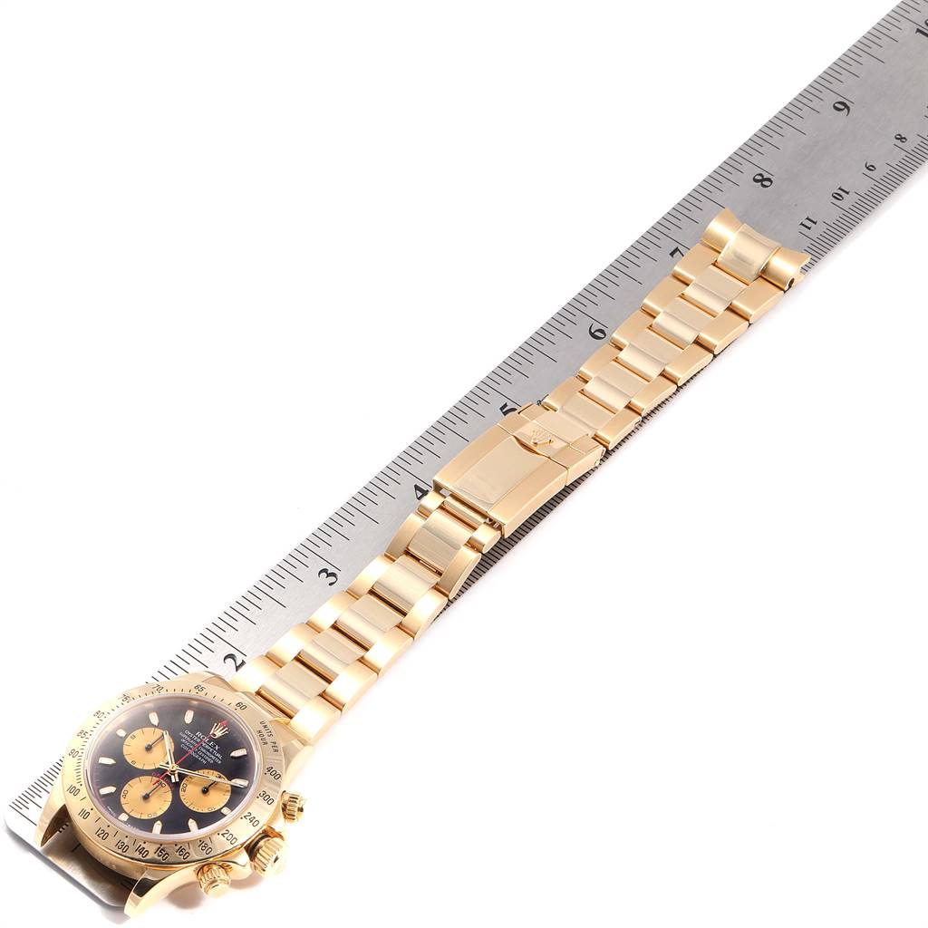 The image shows a Rolex Daytona 116528 Men's Yellow Gold Black Dial 116528 Men's Yellow Gold Black Dial model watch laid flat next to a ruler, displaying the watch's face and bracelet.