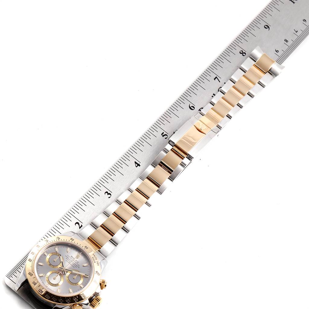 The image shows a Rolex Daytona 116523 Men's Steel and Gold (two tone) Grey Dial 116523 Men's Steel and Gold (two tone) Grey Dial watch laid flat on its side with a ruler beside it, displaying the case and bracelet.