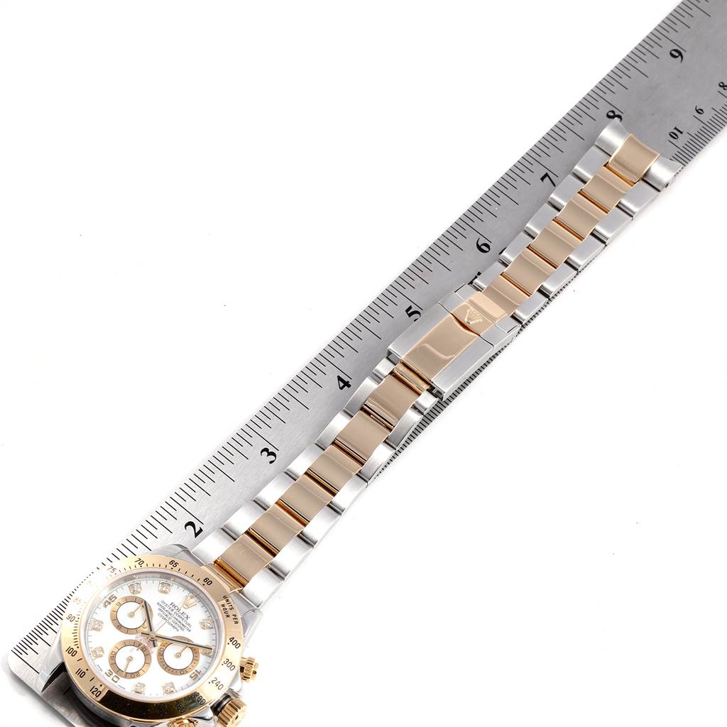 The image shows the Rolex Daytona 116523 Men's Steel and Gold (two tone) White Dial 116523 Men's Steel and Gold (two tone) White Dial watch lying flat next to a ruler, showcasing the strap and part of the dial.