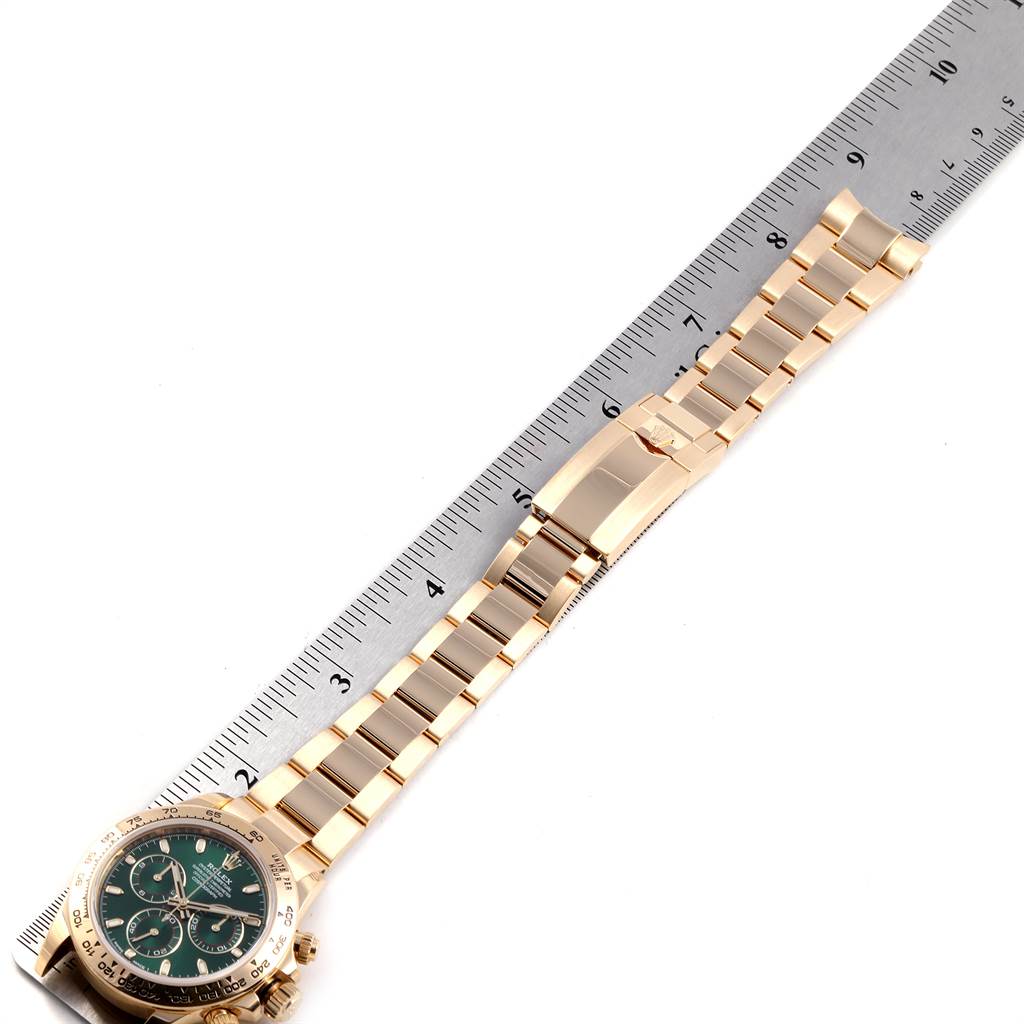 The image shows a Rolex Daytona 116508 Men's Yellow Gold Green Dial 116508 Men's Yellow Gold Green Dial watch positioned horizontally next to a ruler, highlighting the bracelet and clasp.