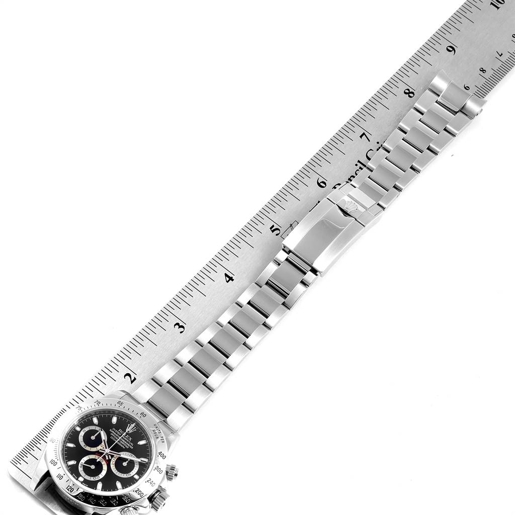 The image shows a Rolex Daytona 116520 Men's Stainless Steel Black Dial 116520 Men's Stainless Steel Black Dial watch laid flat against a ruler, displaying the face and full bracelet.