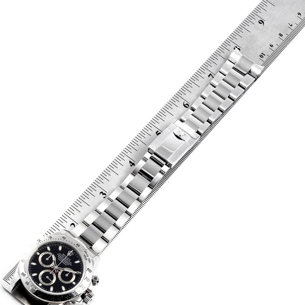 A Rolex Daytona 116520 Men's Stainless Steel Black Dial 116520 Men's Stainless Steel Black Dial watch is shown lying flat with its bracelet partially extended, measured next to a ruler.