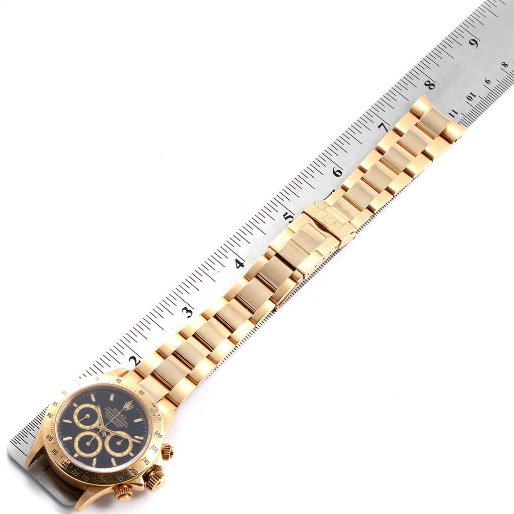 The image shows a golden Rolex Daytona 16528 Men's Yellow Gold Black Dial 16528 Men's Yellow Gold Black Dial watch placed next to a ruler, displaying the watch face and full bracelet from a top-down angle.