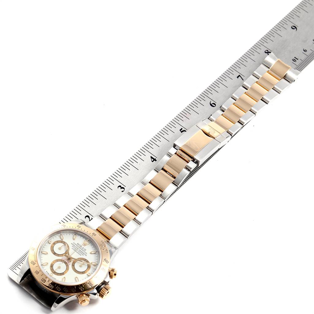 The image shows a top-down view of a Rolex Daytona 116523 Men's Steel and Gold (two tone) White Dial 116523 Men's Steel and Gold (two tone) White Dial watch and its bracelet, accompanied by a ruler for scale.