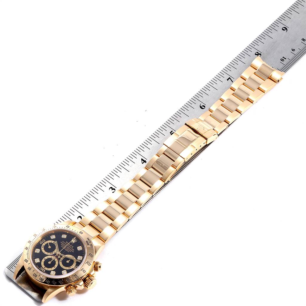 The image shows a Rolex Daytona 16528 Men's Yellow Gold Black Dial 16528 Men's Yellow Gold Black Dial watch laid flat next to a ruler, displaying its gold bracelet and black dial.