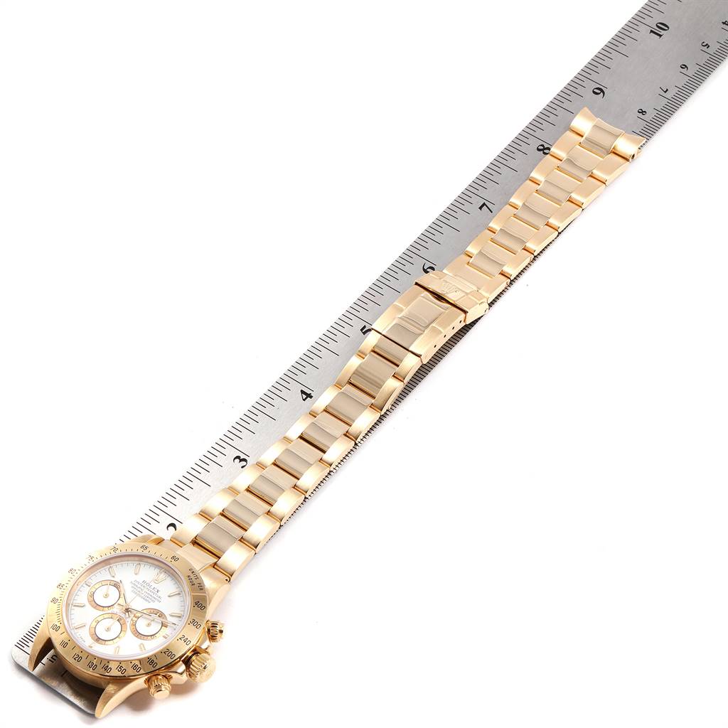 The image shows a gold Rolex Daytona 16528 Men's Yellow Gold White Dial 16528 Men's Yellow Gold White Dial watch laid flat on a ruler, displaying the bracelet and part of the watch face.