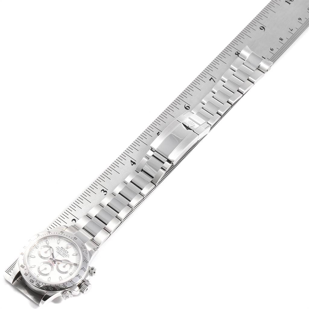 The image shows a top view of a Rolex Daytona 116520 Men's Stainless Steel White Dial 116520 Men's Stainless Steel White Dial watch with its metal bracelet extended alongside a ruler.