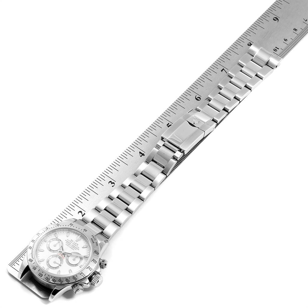 The Rolex Daytona 116520 Men's Stainless Steel White Dial 116520 Men's Stainless Steel White Dial watch is shown from a top-down angle, displaying its entire bracelet and face alongside a ruler.