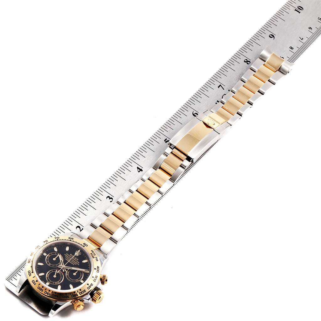 The image shows the Rolex Daytona 116503 Men's Steel and Gold (two tone) Black Dial 116503 Men's Steel and Gold (two tone) Black Dial watch laying flat, measured against a ruler, displaying its face and gold and silver bracelet.