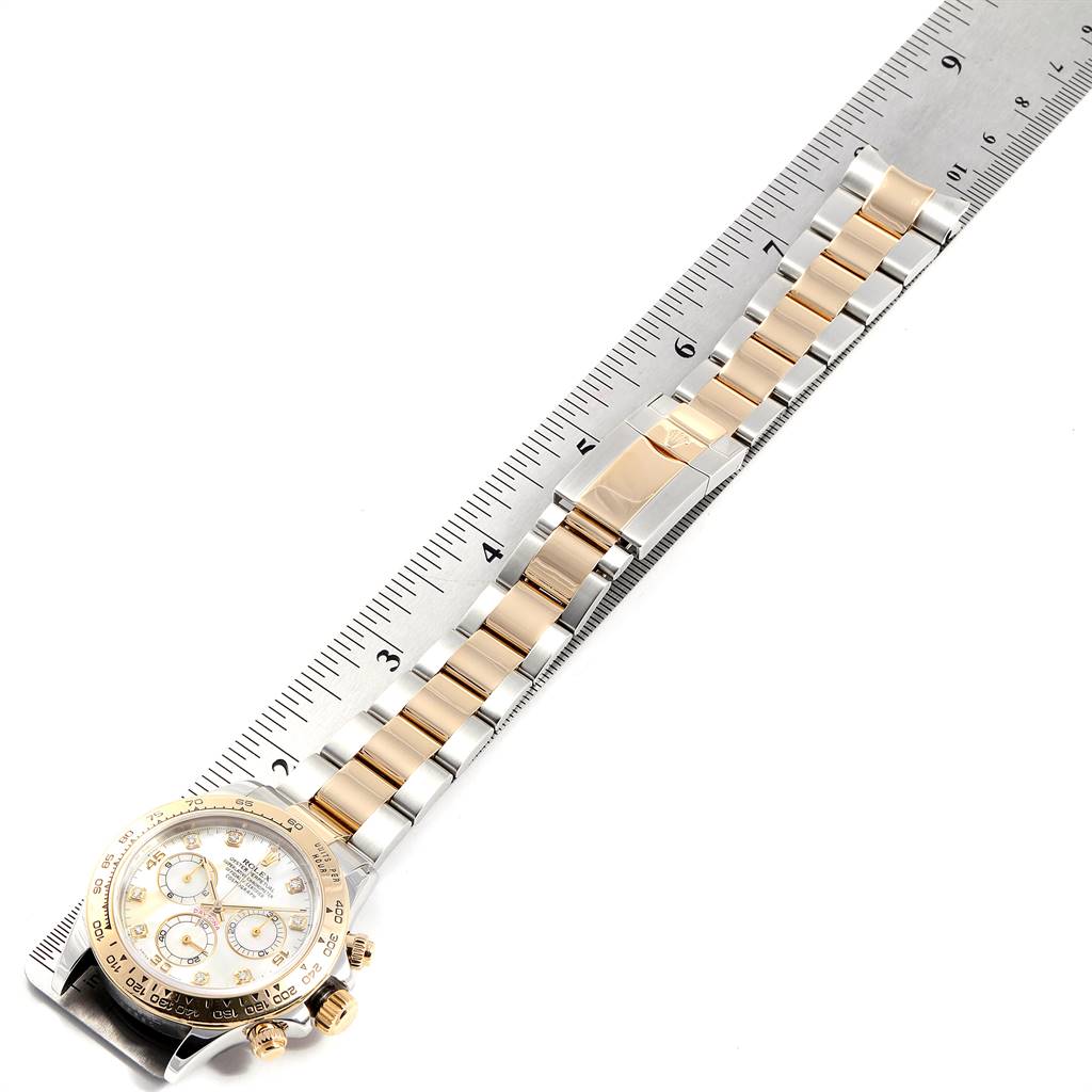 This image shows a Rolex Daytona 116523 Men
s Steel and Gold (two tone) Mother of Pearl Dial 116523 Men
s Steel and Gold (two tone) Mother of Pearl Dial watch laid flat with its strap extended next to a ruler for measurement.