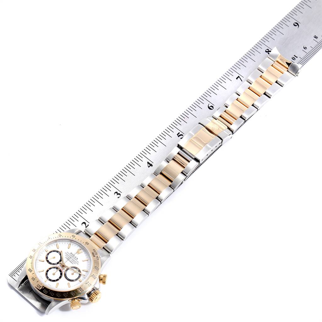 The Rolex Daytona 16523 Men's Steel and Gold (two tone) White Dial 16523 Men's Steel and Gold (two tone) White Dial watch is shown at a diagonal angle, highlighting the face, bezel, and bracelet beside a ruler.