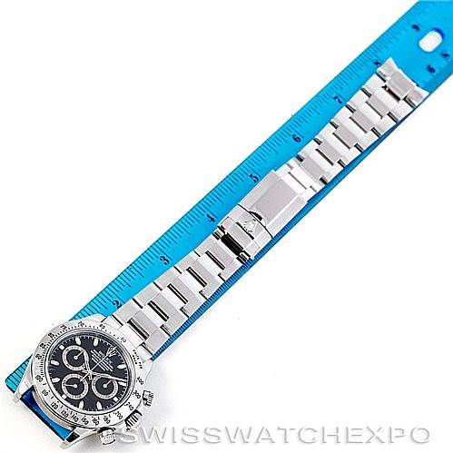 The Rolex Daytona 116520 Men's Stainless Steel Black Dial 116520 Men's Stainless Steel Black Dial watch is shown from a top-down angle, displaying the watch face, bracelet, and clasp beside a blue ruler.