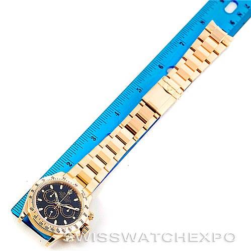 The image shows a Rolex Daytona 116528 Men's Yellow Gold Black Dial 116528 Men's Yellow Gold Black Dial watch positioned horizontally next to a blue ruler, displaying the entire bracelet and part of the watch dial.