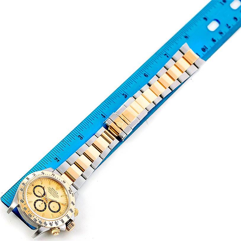 The image shows a Rolex Daytona 16523 Men's Steel and Gold (two tone) Champagne Dial 16523 Men's Steel and Gold (two tone) Champagne Dial watch laid flat, with its bracelet aligned against a blue ruler for measurement.