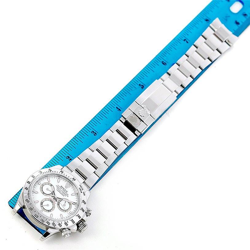 The Rolex Daytona 116520 Men's Stainless Steel White Dial 116520 Men's Stainless Steel White Dial watch is shown from an angled top view, with the entire watch and bracelet displayed alongside a ruler for scale.