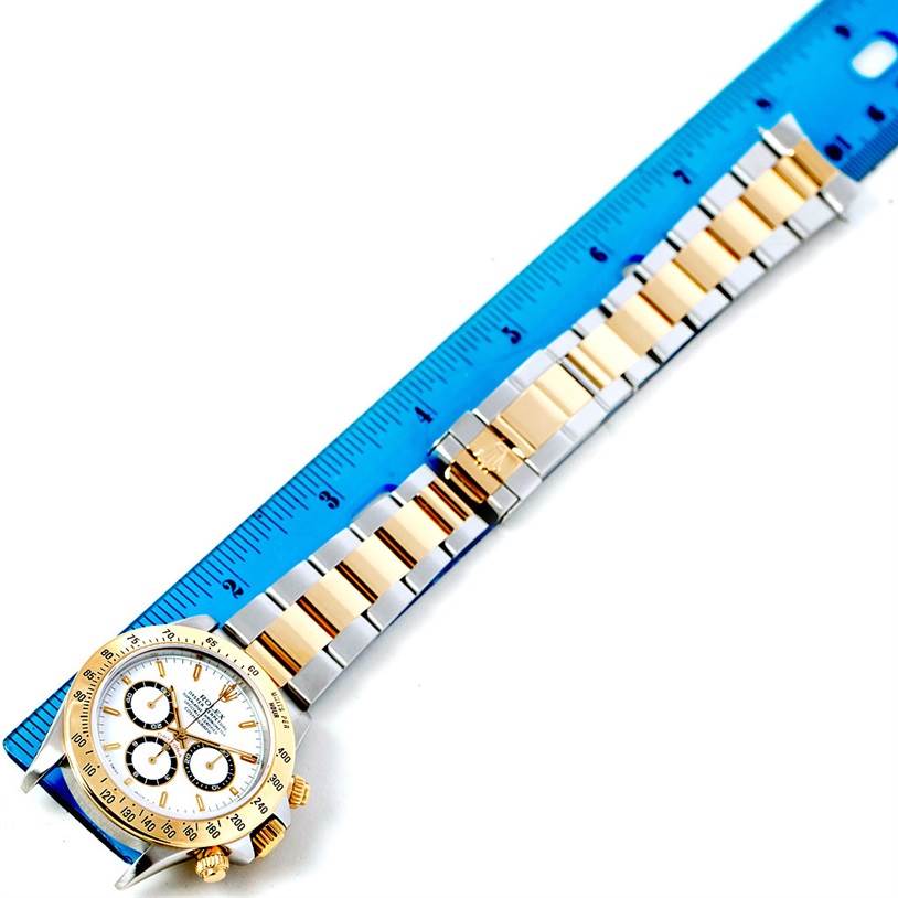 The image shows a Rolex Daytona 16523 Men's Steel and Gold (two tone) White Dial 16523 Men's Steel and Gold (two tone) White Dial watch laid flat with its bracelet extended alongside a blue ruler for measurement.