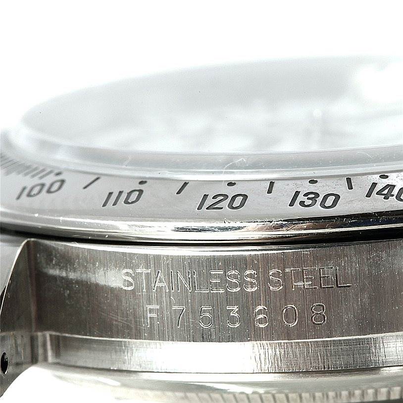 The close-up image shows part of the bezel and case of a Rolex Daytona 116520 Men
s Stainless Steel White Dial 116520 Men
s Stainless Steel White Dial watch, highlighting its stainless steel and engraved serial number.