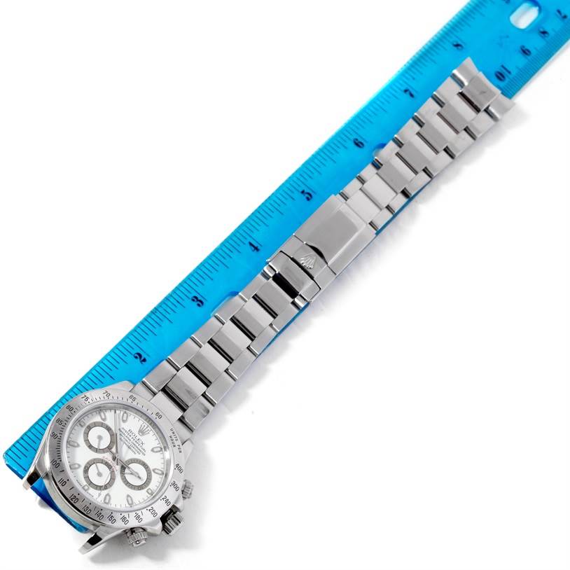 The Rolex Daytona 116520 Men's Stainless Steel White Dial 116520 Men's Stainless Steel White Dial watch is shown from a top-down angle, displaying the face, bezel, bracelet, and clasp, next to a ruler.