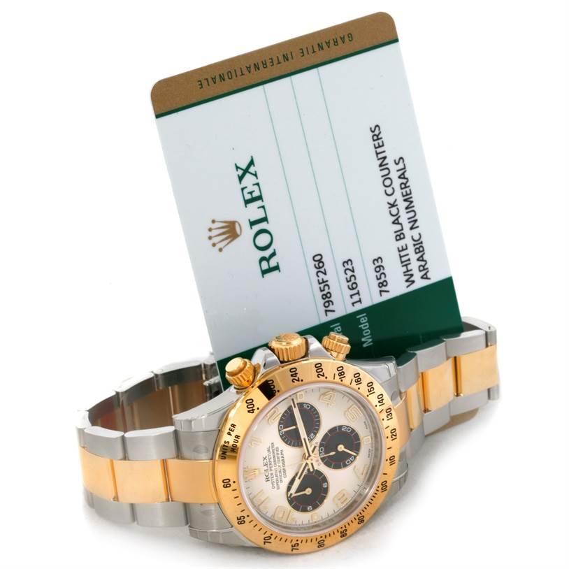 This image shows a Rolex Daytona 116523 Men's Steel and Gold (two tone) White Dial 116523 Men's Steel and Gold (two tone) White Dial watch in a side angle along with its warranty card.