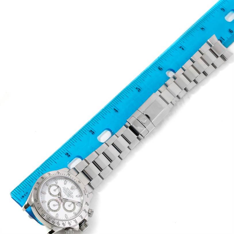 The image shows a Rolex Daytona 116520 Men's Stainless Steel White Dial 116520 Men's Stainless Steel White Dial watch laid flat with its clasp and bracelet aligned alongside a ruler for measurement.