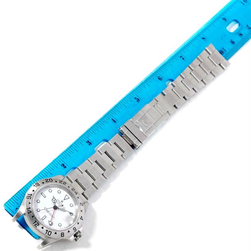 The Rolex Explorer 16570 Men's Stainless Steel White Dial 16570 Men's Stainless Steel White Dial watch is shown from a top-down angle, with its face, bezel, and metal bracelet visible, placed next to a ruler.