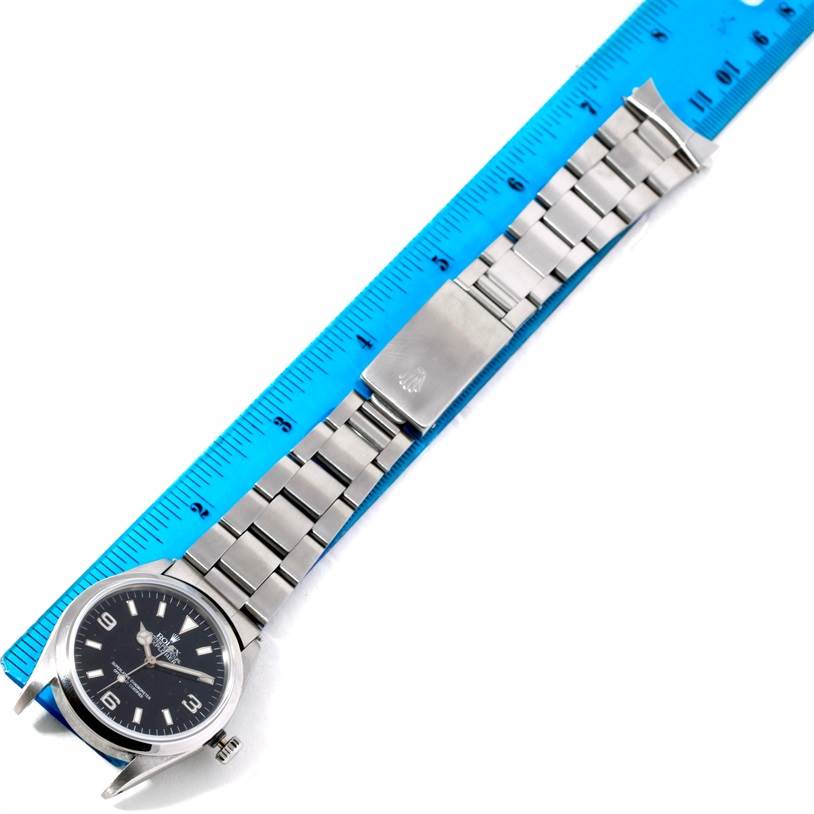 This image shows a Rolex Explorer 14270 Men's Stainless Steel Black Dial 14270 Men's Stainless Steel Black Dial watch with a stainless steel bracelet laid flat next to a blue measuring ruler.