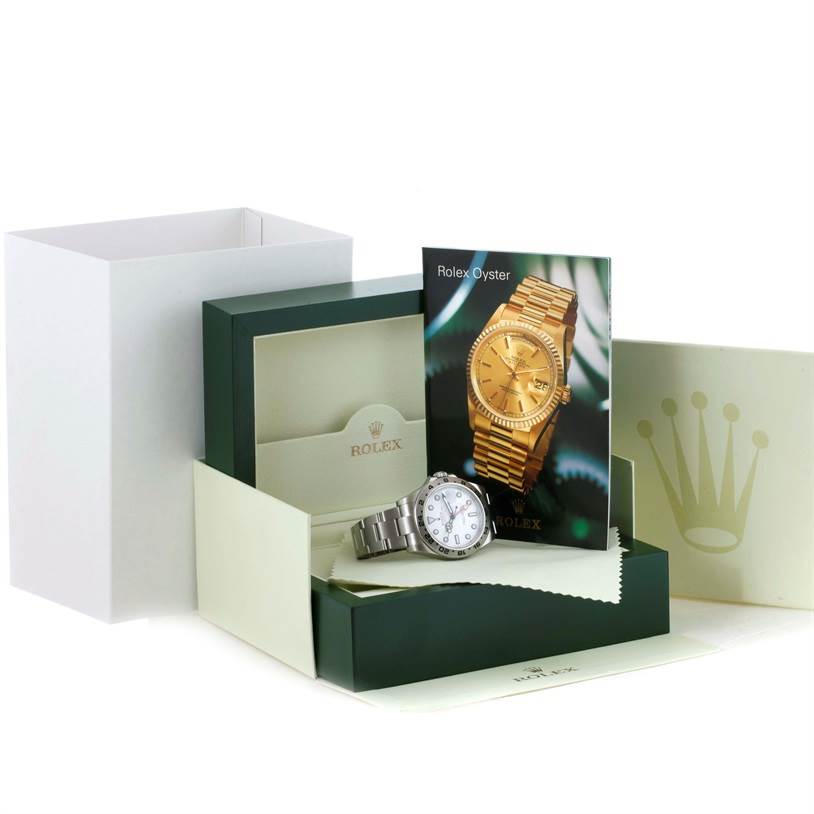 The image shows a Rolex Explorer 216570 Men
s Stainless Steel White Dial 216570 Men
s Stainless Steel White Dial model watch from an angled top view, along with its box, warranty card, and booklets.