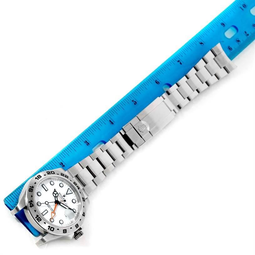 The image shows a side view of the Rolex Explorer 216570 Men
s Stainless Steel White Dial 216570 Men
s Stainless Steel White Dial watch placed alongside a blue ruler, displaying its metal bracelet and clasp.