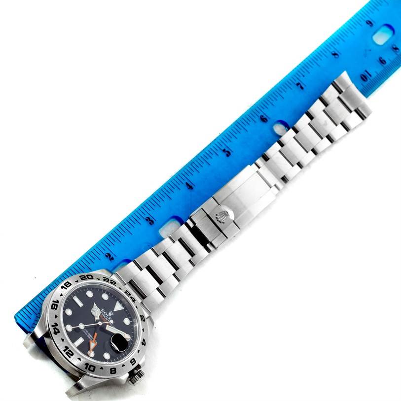 This image shows a Rolex Explorer 216570 Men
s Stainless Steel Black Dial 216570 Men
s Stainless Steel Black Dial watch laid flat next to a blue ruler, highlighting the dial, bezel, and metal bracelet.