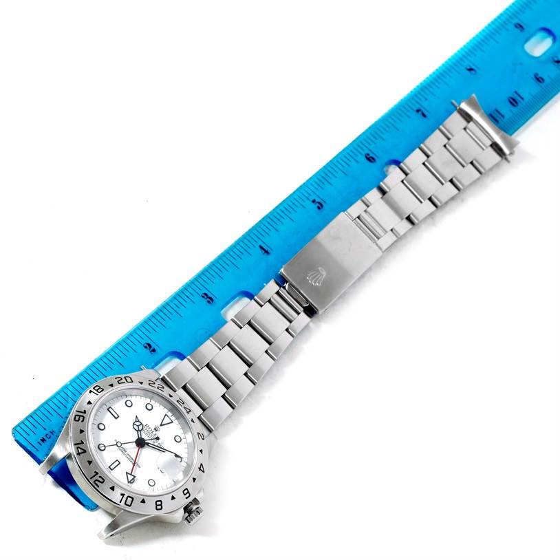 The Rolex Explorer 16570 Men's Stainless Steel White Dial 16570 Men's Stainless Steel White Dial watch is shown laid flat alongside a ruler, displaying the face, bezel, and bracelet with clasp.