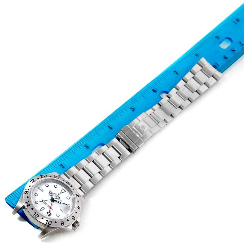 The image shows a Rolex Explorer 16570 Men's Stainless Steel White Dial 16570 Men's Stainless Steel White Dial watch laid flat, with its stainless steel strap extended beside a blue ruler.