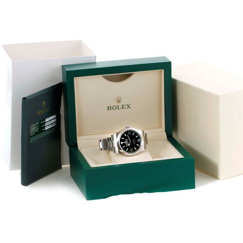 The image shows the Rolex Explorer 214270 Men's Stainless Steel Black Dial 214270 Men's Stainless Steel Black Dial model watch in its open box alongside its outer box and accompanying paperwork.