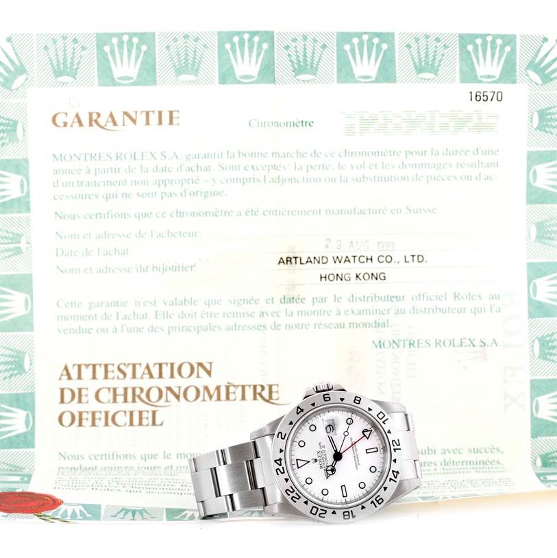 The image shows a Rolex Explorer 16570 Men's White Dial 16570 Men's White Dial watch positioned on top of its official warranty certificate.