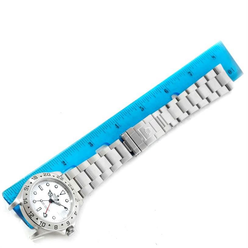 The Rolex Explorer 16570 Men's Stainless Steel White Dial 16570 Men's Stainless Steel White Dial watch is shown from an angled top view, highlighting the dial, bezel, bracelet, and clasp next to a ruler.