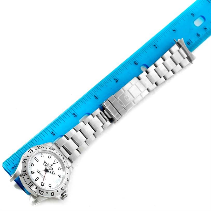 This image shows a Rolex Explorer 16570 Men
s Stainless Steel White Dial 16570 Men
s Stainless Steel White Dial watch laid flat next to a blue ruler, highlighting its bracelet and clasp.