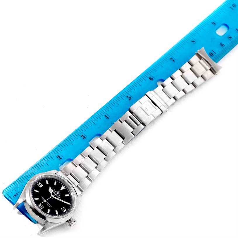 The image shows a top-down view of a Rolex Explorer 14270 Men's Stainless Steel Black Dial 14270 Men's Stainless Steel Black Dial watch with a blue ruler alongside its metal bracelet.