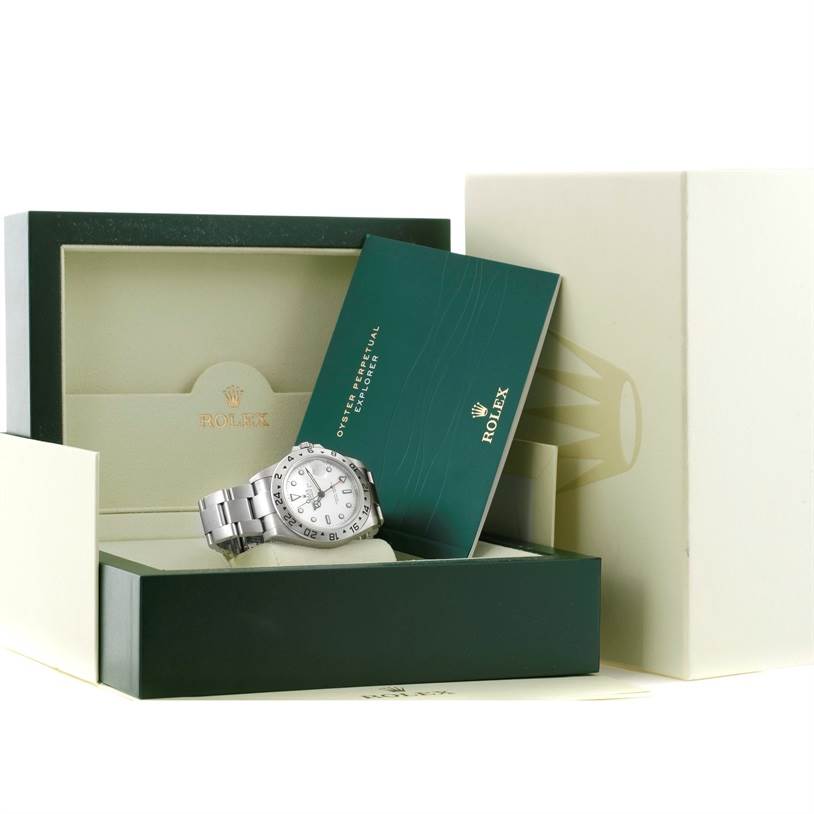The image shows a Rolex Explorer 16570 Men
s Stainless Steel White Dial 16570 Men
s Stainless Steel White Dial watch, partially out of its box, along with accompanying documents and packaging.