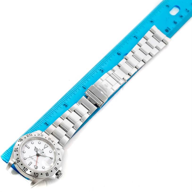 The image shows the Rolex Explorer 16570 Men
s Stainless Steel White Dial 16570 Men
s Stainless Steel White Dial watch laid flat along a blue ruler, displaying its face, bracelet, and clasp.