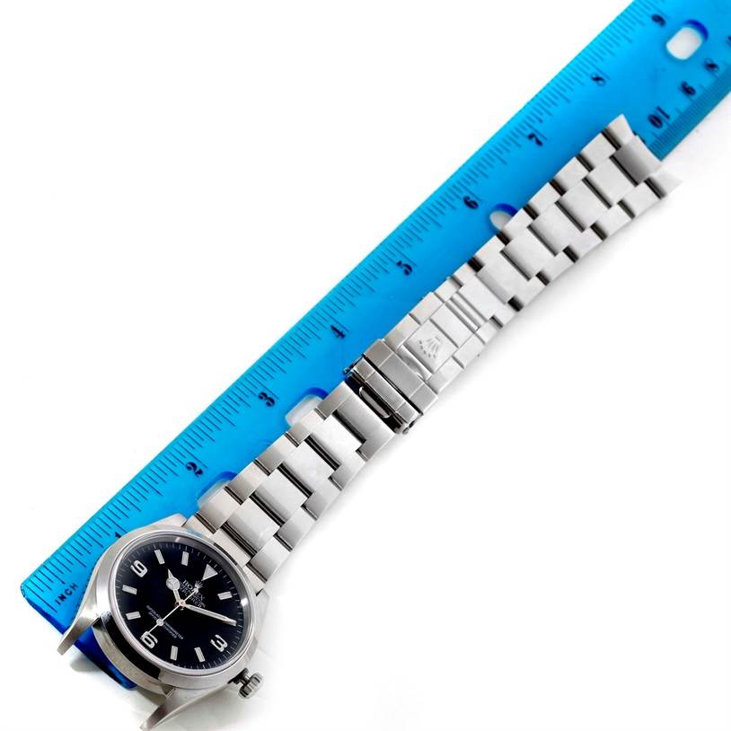 This image shows a Rolex Explorer 114270 Men's Stainless Steel Black Dial 114270 Men's Stainless Steel Black Dial model watch laid flat next to a blue ruler, displaying the watch face and metal strap.