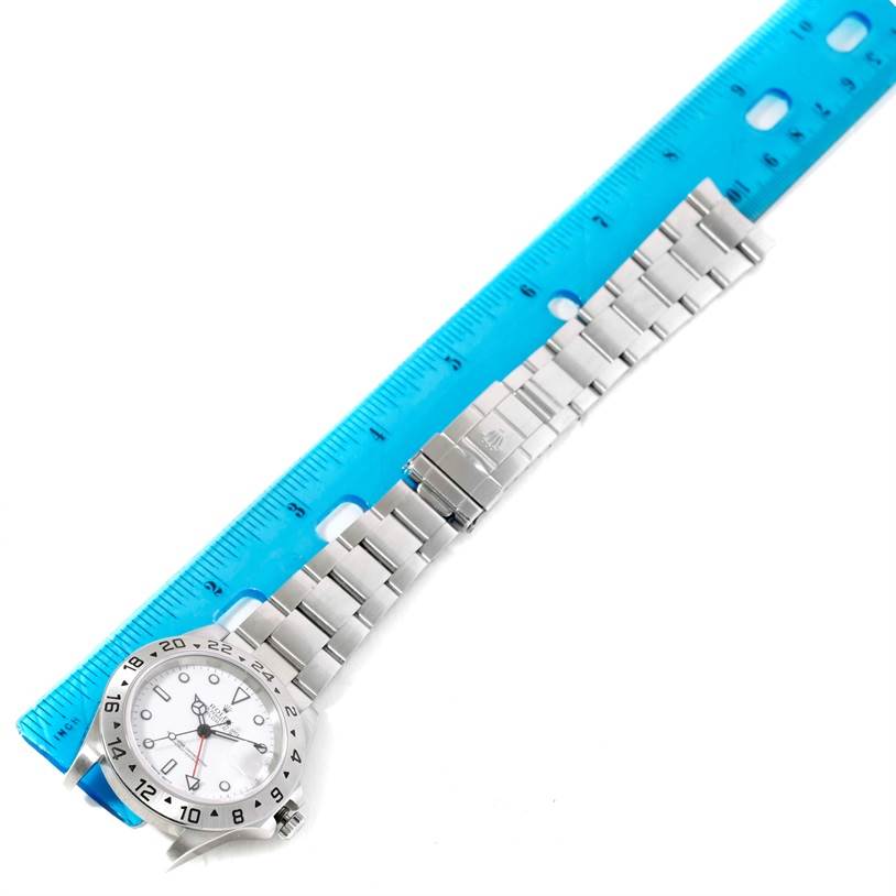 The Rolex Explorer 16570 Men's Stainless Steel White Dial 16570 Men's Stainless Steel White Dial watch is shown lying flat with the dial, bezel, bracelet, and clasp visible, alongside a blue ruler.