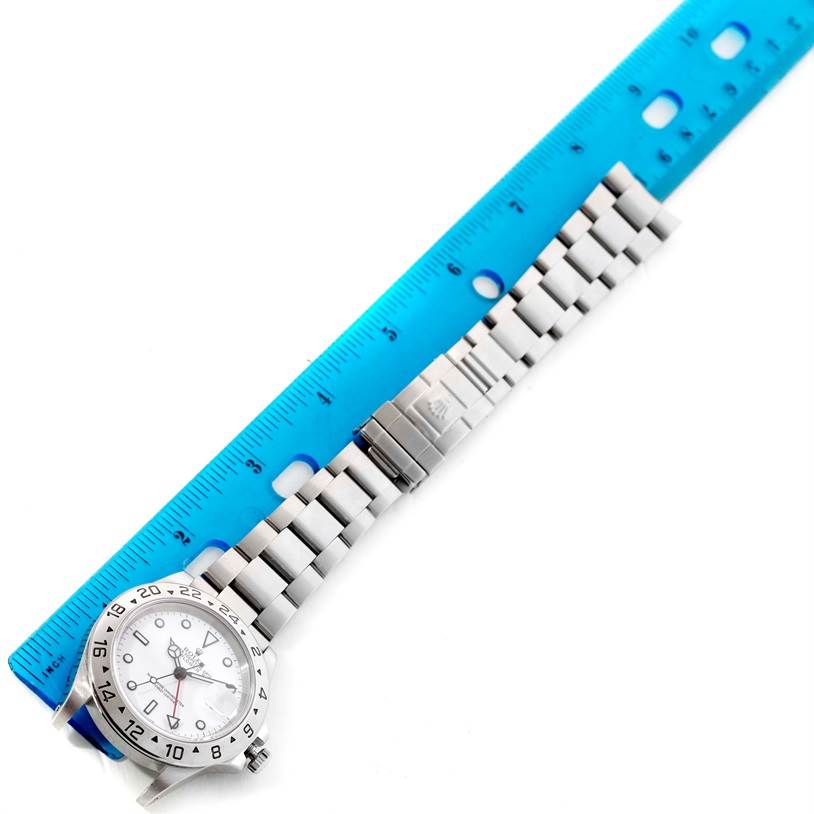 The image shows a Rolex Explorer 16570 Men's Stainless Steel White Dial 16570 Men's Stainless Steel White Dial watch with a metal bracelet strap measured against a blue ruler.