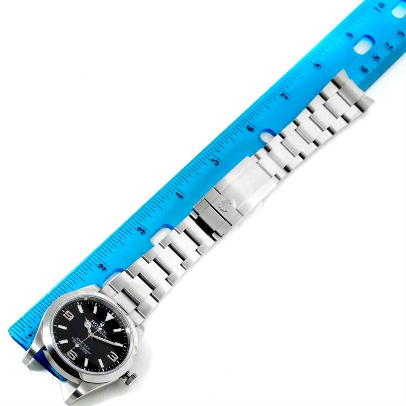 The image shows a Rolex Explorer 214270 Men's Stainless Steel Black Dial 214270 Men's Stainless Steel Black Dial watch placed next to a blue ruler, displaying its face and metal bracelet.