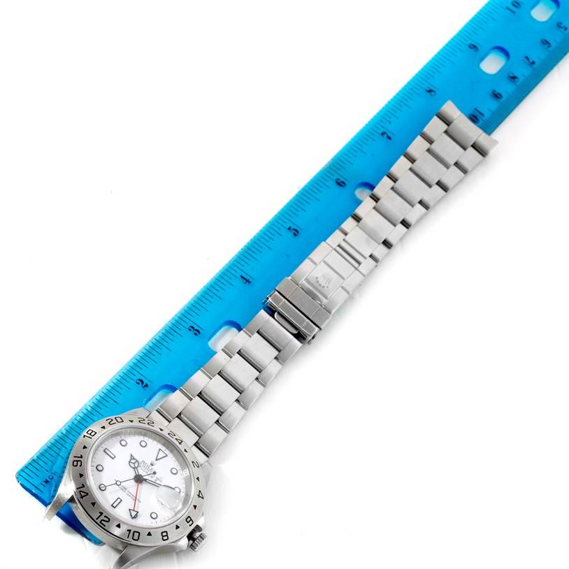 The image shows a Rolex Explorer 16570 Men's Stainless Steel White Dial 16570 Men's Stainless Steel White Dial watch laid out flat next to a blue ruler, displaying the watch face, bracelet, and clasp.