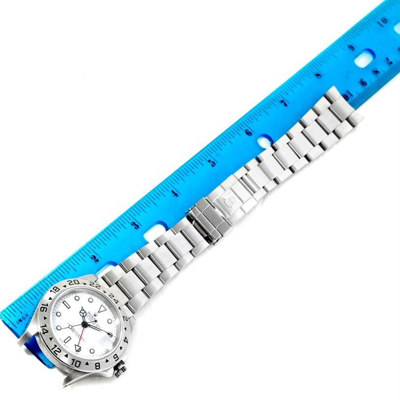 The image shows a Rolex Explorer 16570 Men's Stainless Steel White Dial 16570 Men's Stainless Steel White Dial watch lying flat next to a blue ruler, highlighting its length and stainless steel bracelet.